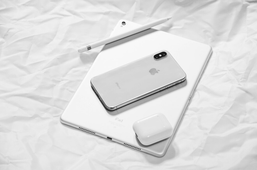 Flat lay of a smartphone, tablet, charging cable, glasses and a notebook with handwritten instructions on a pastel desk