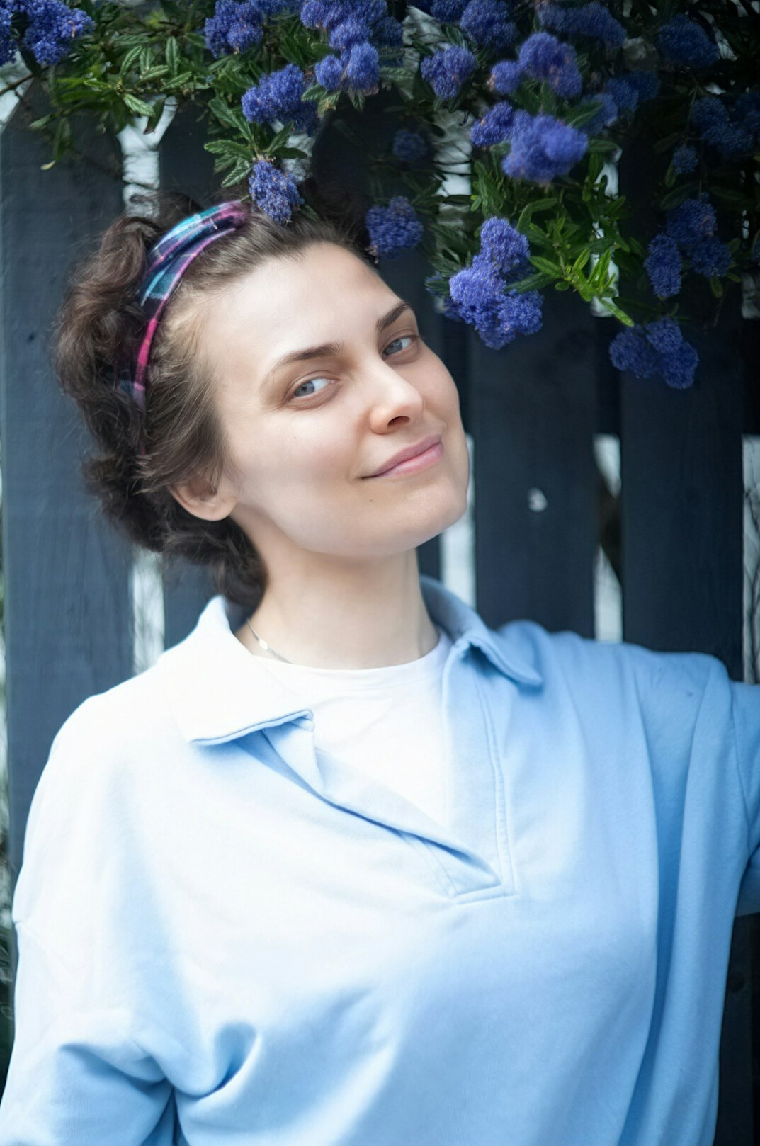 Portrait of a smiling 38 year old woman with brown shoulder-length hair wearing a light blue blouse