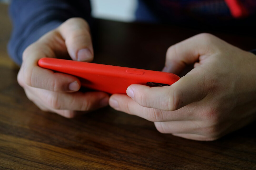 Close-up of hands holding a modern smartphone over a wooden table with a notebook and a cup of tea