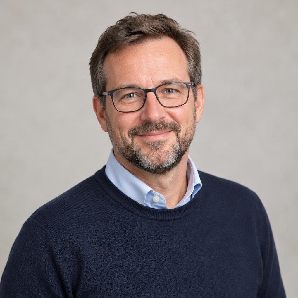 Portrait of a friendly 45 year old man with a short beard and glasses wearing a navy sweater